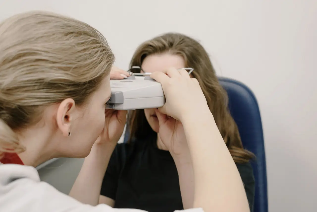 Unrecognizable ophthalmologist examining eyesight of woman with vision device