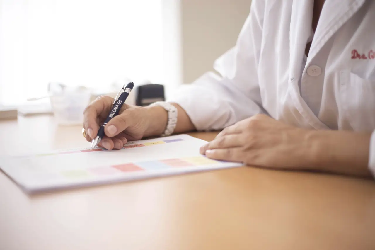 Close-up of a Doctor Sitting at a Desk and Writing on Paper